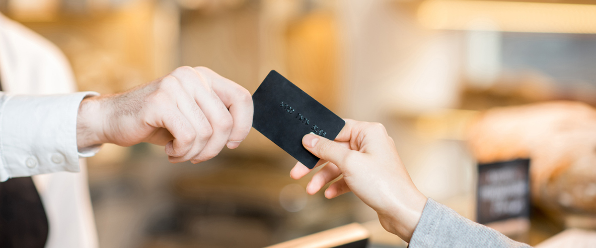 a black debit card being exchanged from one person's hand to another person's hand